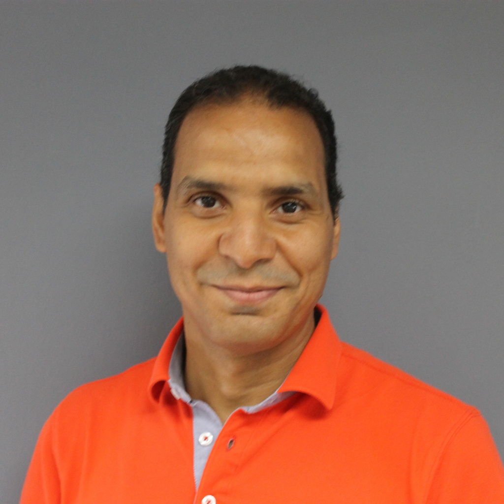 young brown skinned man with short hair, wearing an orange shirt, slight smile 
